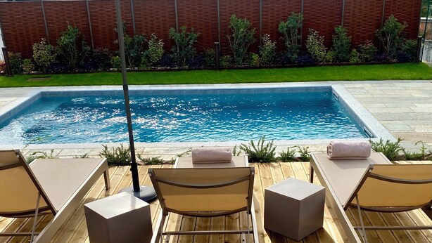 A poolside area with a rectangular pool, wooden deck, and lounge chairs with cushions. - Corte San Martino (La Morra)