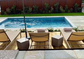 A poolside area with a rectangular pool, wooden deck, and lounge chairs with cushions. - Corte San Martino (La Morra)