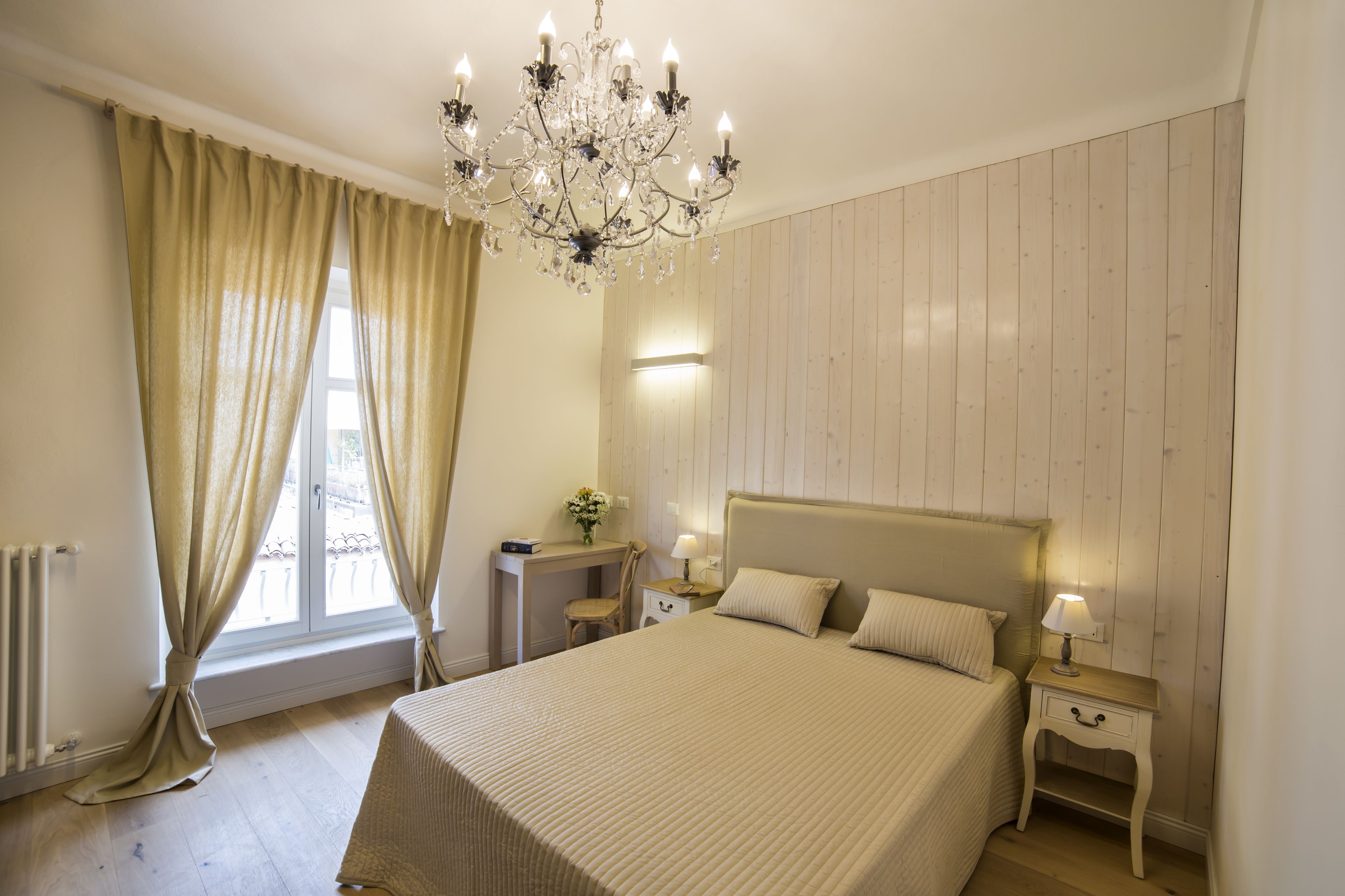 Ein Schlafzimmer mit einem großen Bett, einem Nachttisch mit Lampe, einem Schreibtisch mit Stuhl und einem Fenster mit Vorhängen.