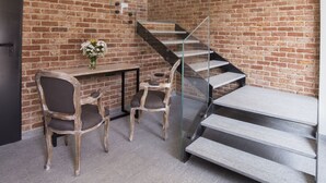 A modern interior with a brick wall, a staircase with glass railings, and a wooden desk with chairs. - Corte San Martino (La Morra)