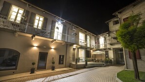A courtyard with a paved walkway, potted plants, outdoor seating, and a building with multiple balconies and windows. - Corte San Martino (La Morra)