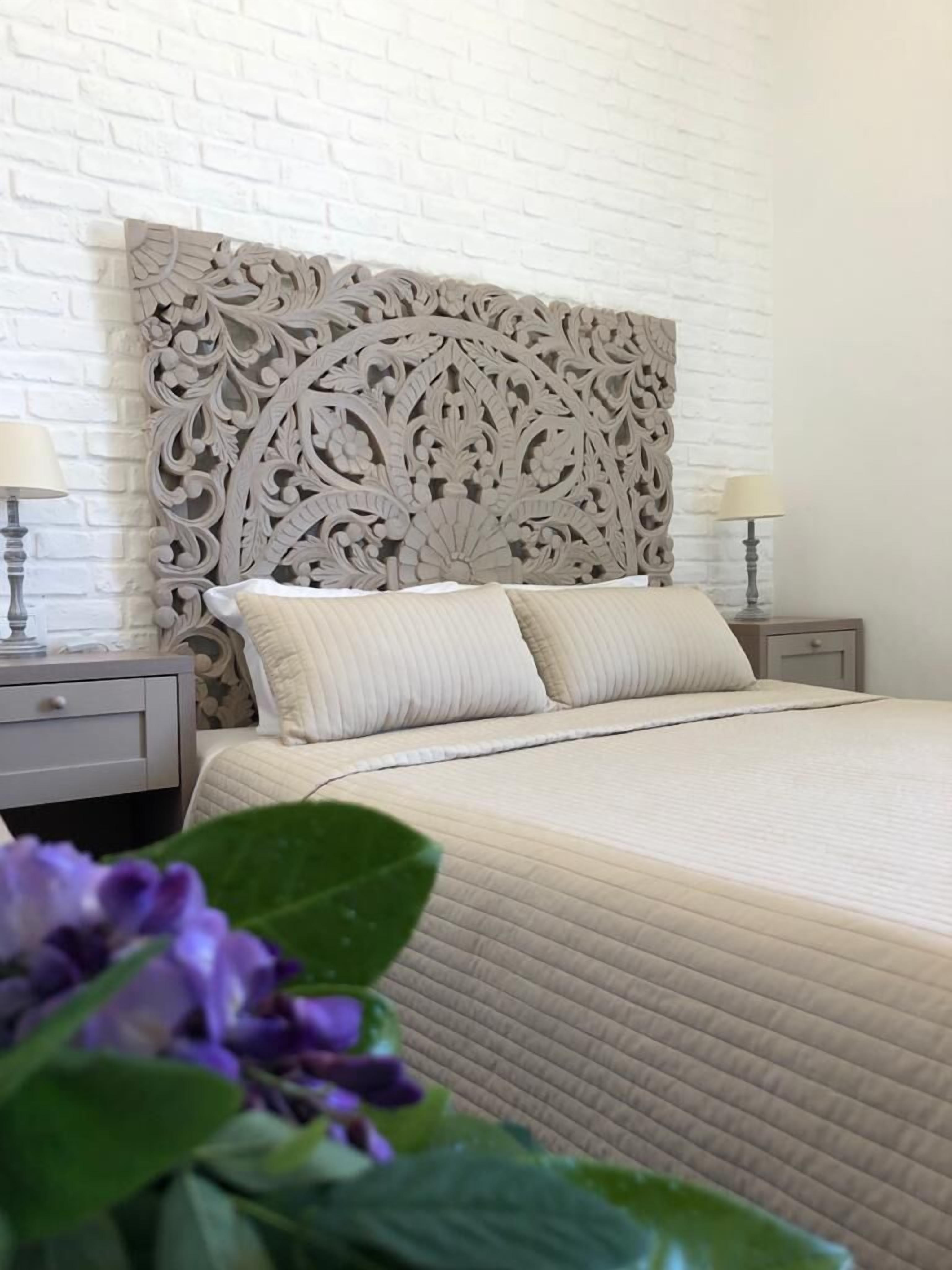 Une chambre à coucher avec une tête de lit décorative, un lit avec deux oreillers, une table de chevet avec une lampe et une commode.