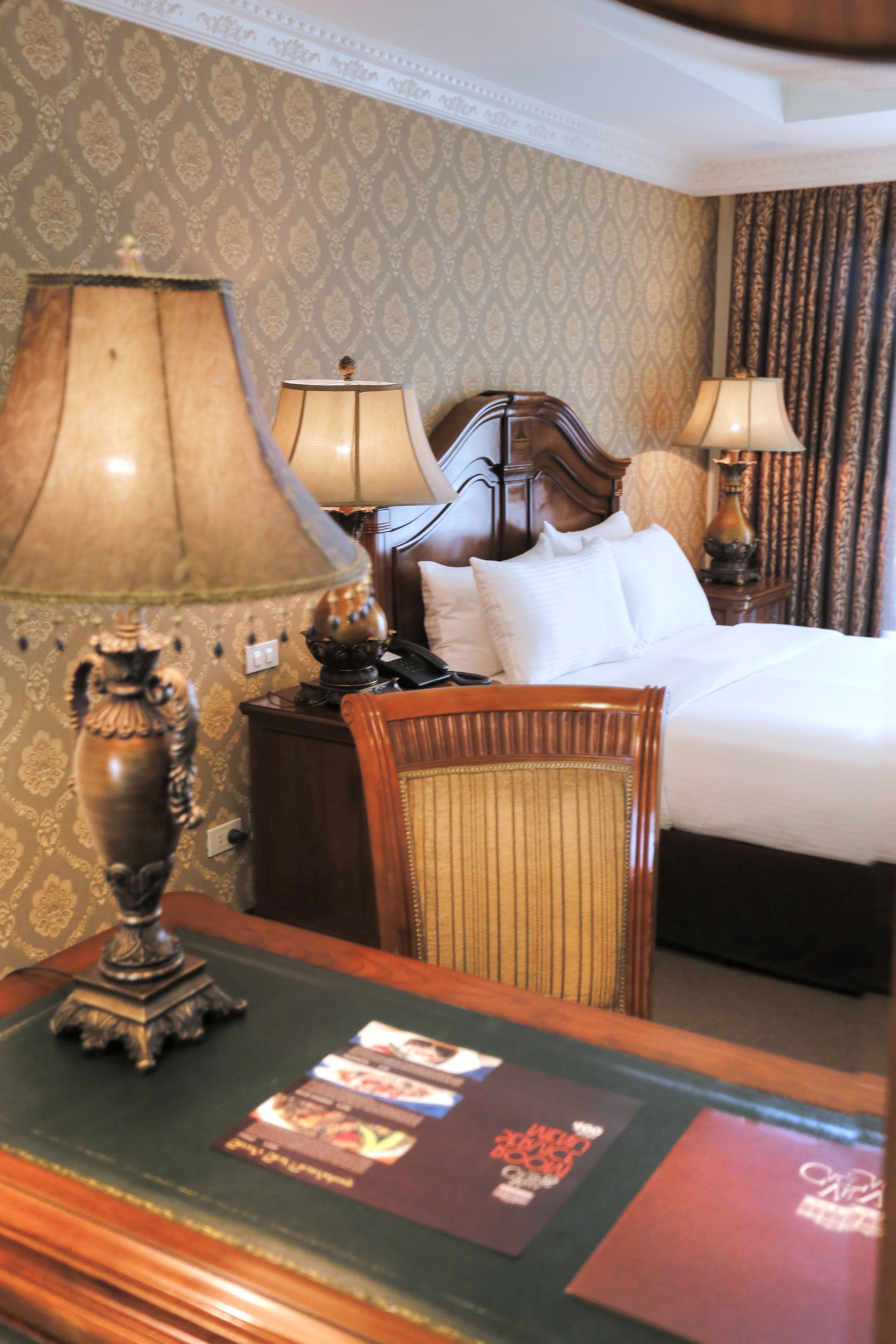Een hotelkamer met een bed, twee bedlampen, een houten nachtkastje en een stoel.