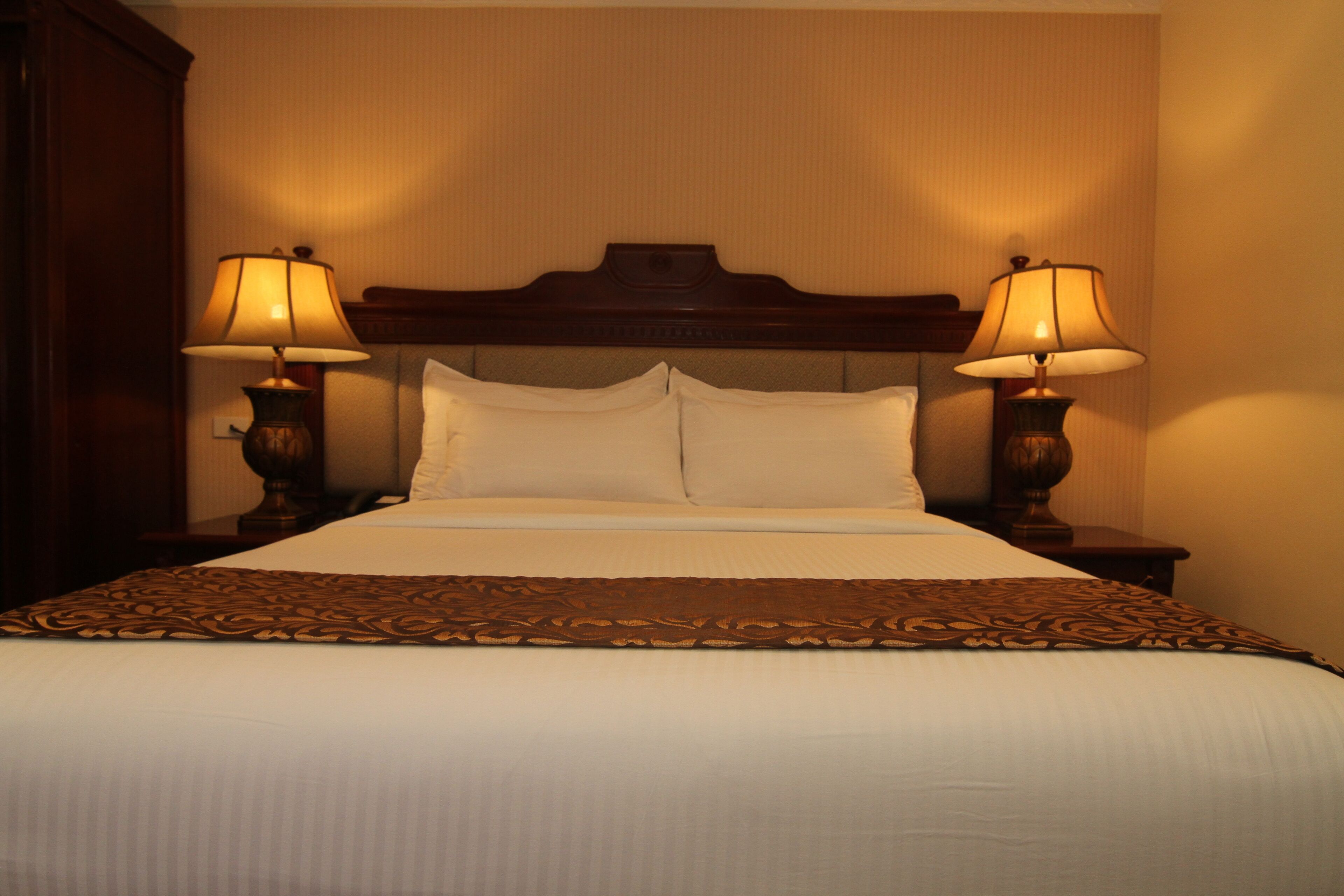 A neatly made bed with a wooden headboard, two bedside lamps, and a decorative bed runner.
