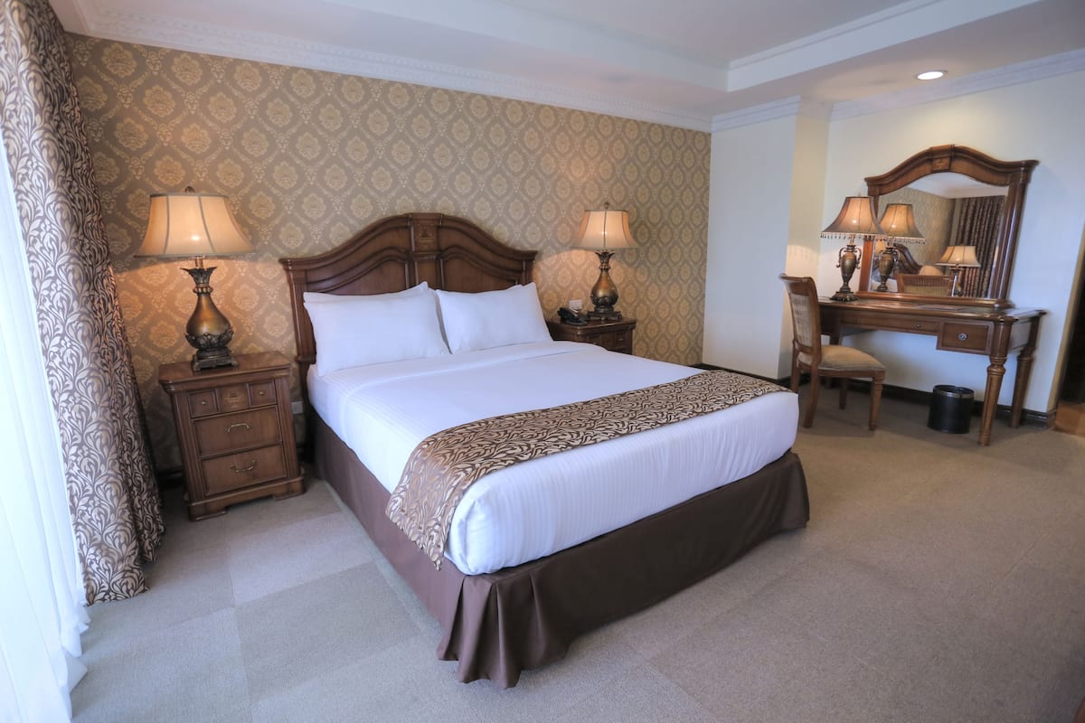 Una habitación de hotel con una cama grande, dos mesitas de noche con lámparas, un aparador de madera y un espejo.