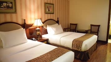 A hotel room with two beds, a nightstand with a lamp, a chair, and a small table.