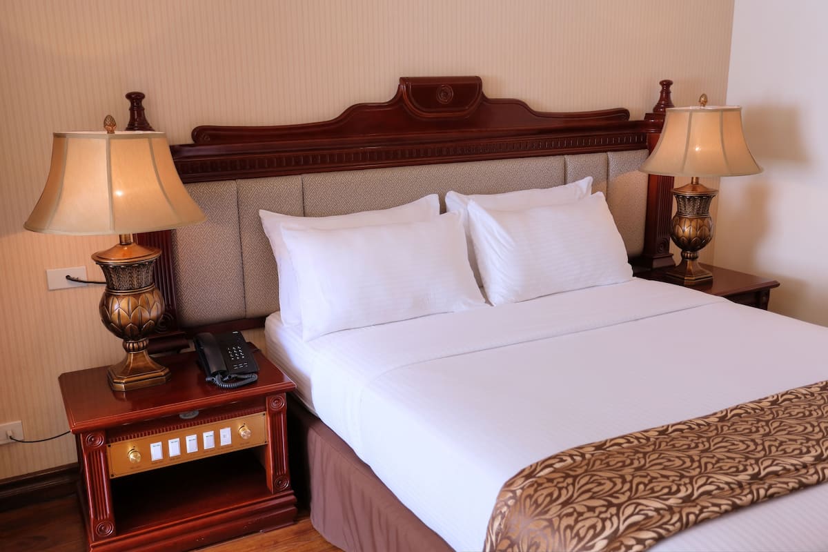 Una habitación de hotel con una cama grande, dos mesitas de noche, un teléfono y dos lámparas.