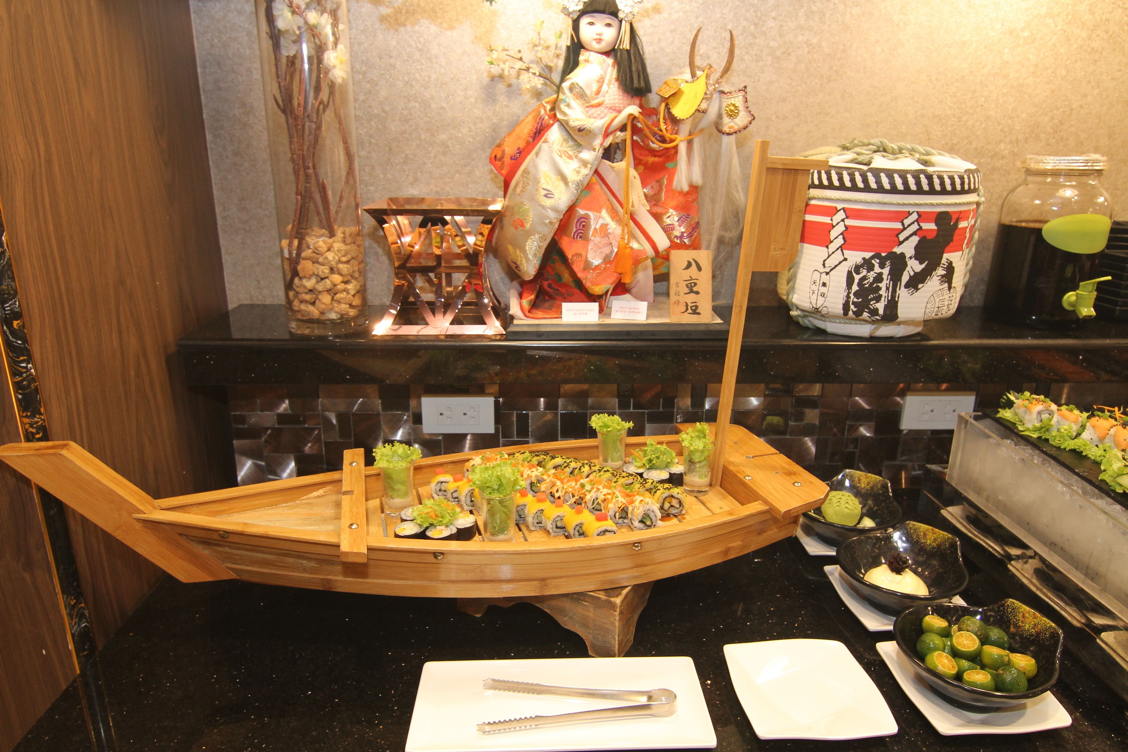 A sushi bar with a wooden boat display, a decorative doll, and various condiments.
