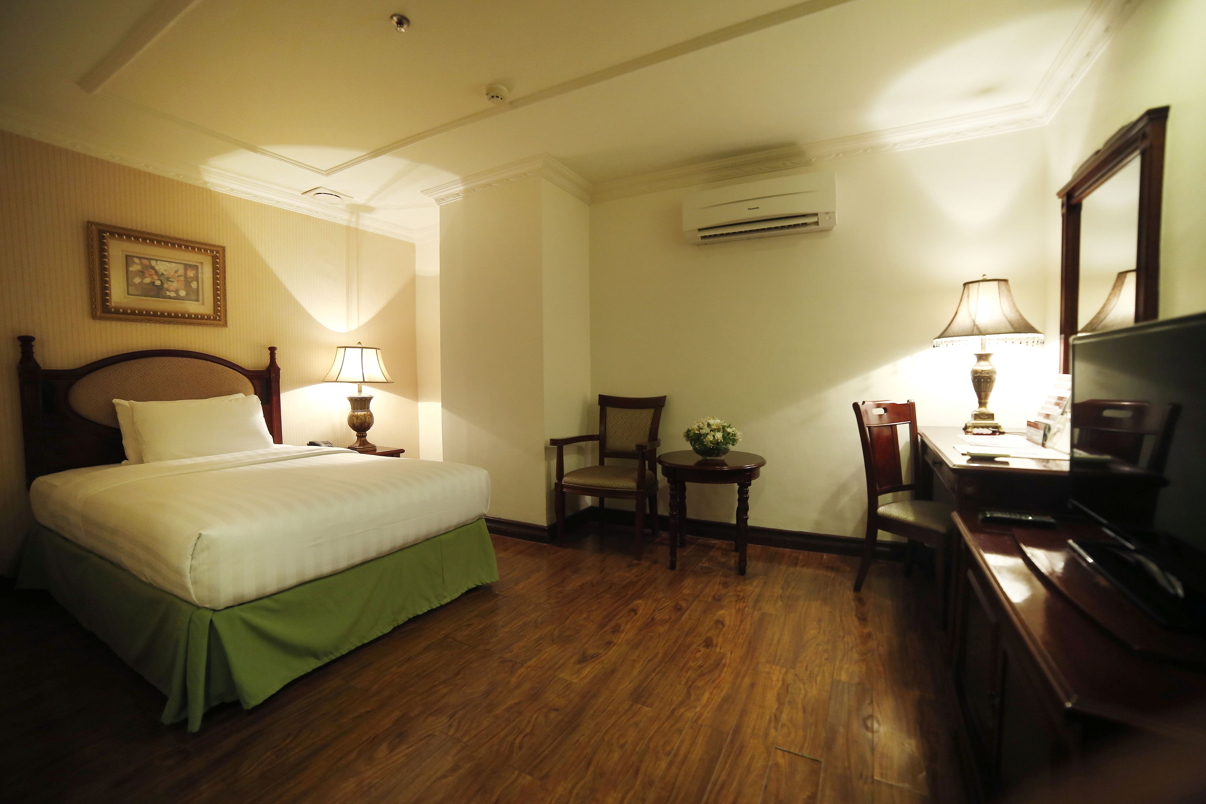 Una habitación de hotel con cama, escritorio, silla, televisor y aire acondicionado.