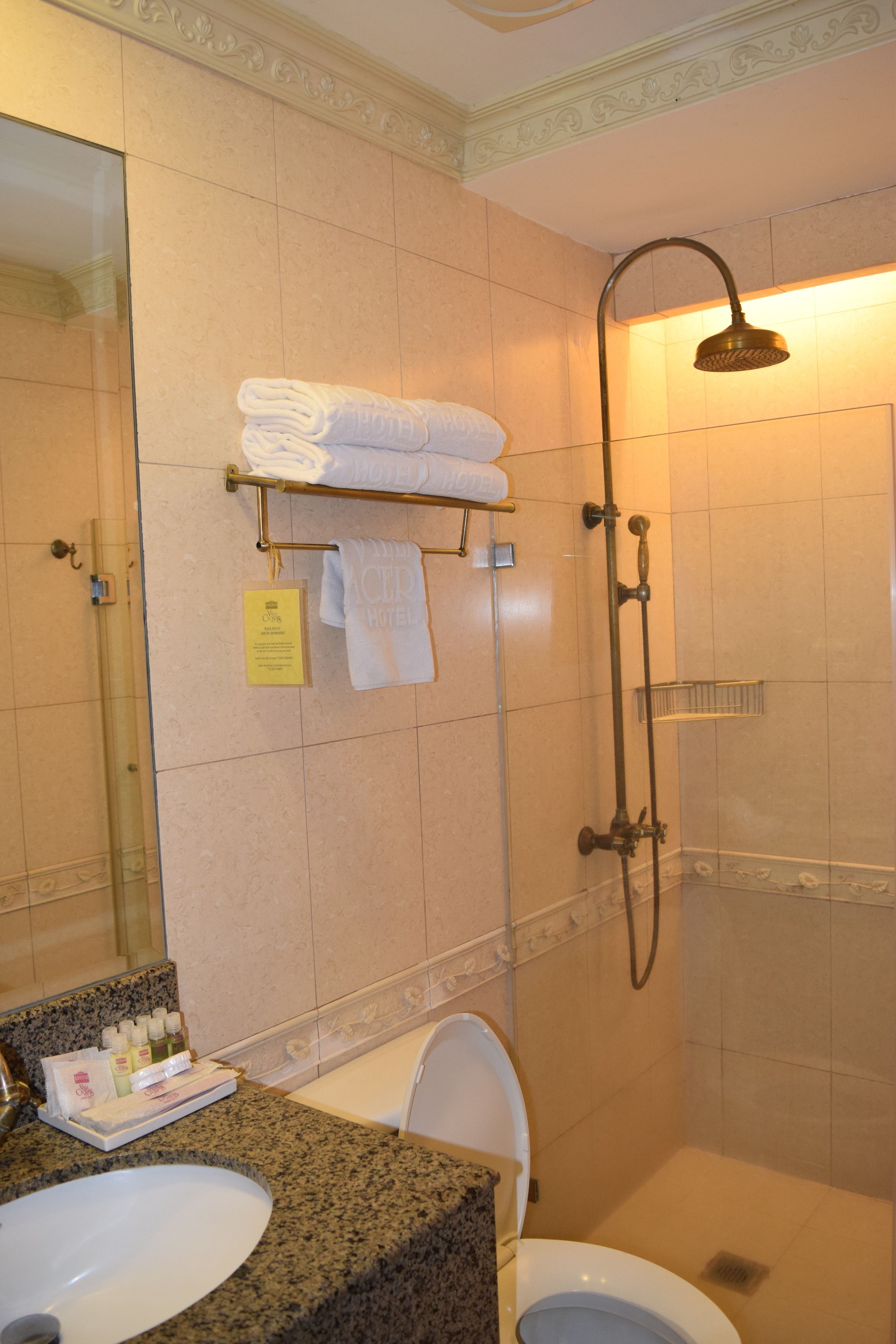 Une salle de bain avec un lavabo, des toilettes et une douche. Des serviettes sont suspendues sur un porte-serviettes, et des articles de toilette sont posés sur le comptoir.