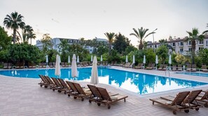 A swimming pool with lounge chairs and umbrellas, surrounded by greenery and buildings. - Pine House by Werde Hotels - All inclusive (Kemer)