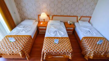 Habitación de hotel con tres camas individuales, cada una con una colcha estampada y almohada bien ordenada. Hay una mesita de noche con lámpara entre las camas, y un teléfono en la mesita de noche derecha.