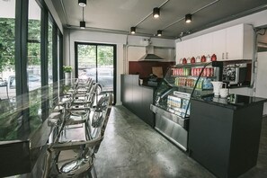 A modern restaurant interior with a long counter, a glass display case with beverages, and a view of the street outside. - Nourish Vegan B&B (Chiang Mai)