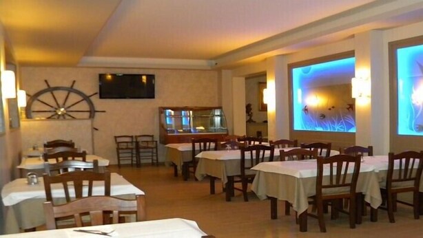 Ein Restaurant mit mehreren Tischen und Stühlen, einer großen Schiffslenken-Dekoration an der Wand und einem Bildschirm, der eine fischbezogene Animation zeigt.
