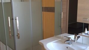Ein modernes Badezimmer mit einer Duschkabine aus Glas, einem weißen Waschbecken und einem Spiegel darüber.
