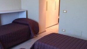 Ein Zimmer mit zwei Einzelbetten, einem weißen Regal und einer Tür zu einem anderen Raum.