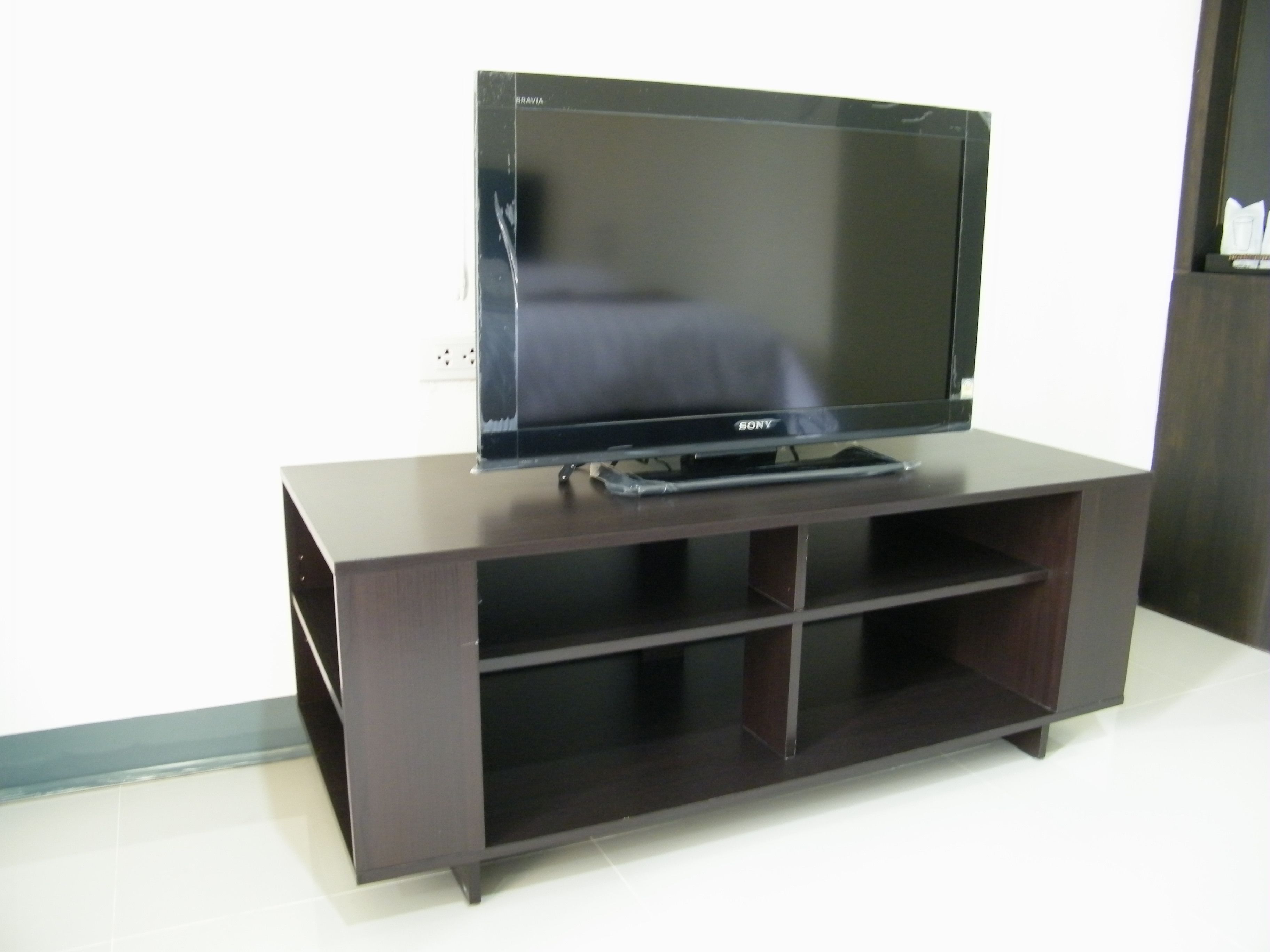 A flat-screen TV on a wooden TV stand with a shelf below.