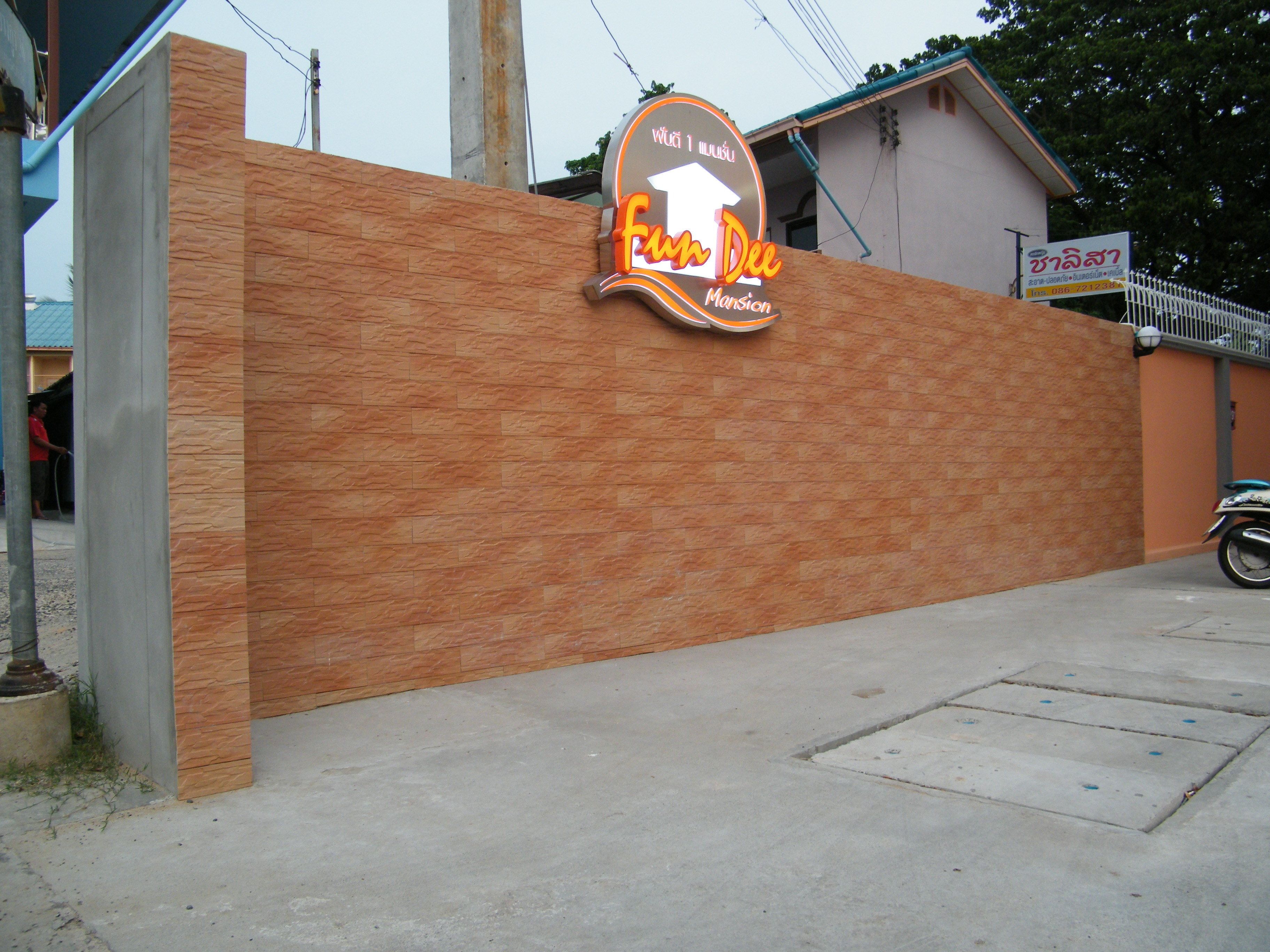 A sign for 'Fun Dee Mansion' with a brick wall and a motorcycle parked nearby.