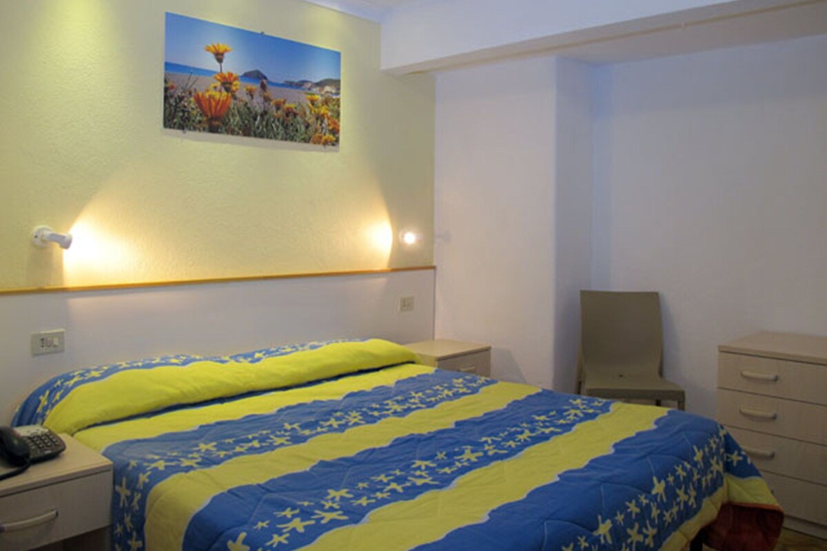 A bedroom with two beds, a nightstand, a desk, a chair, and a painting on the wall.