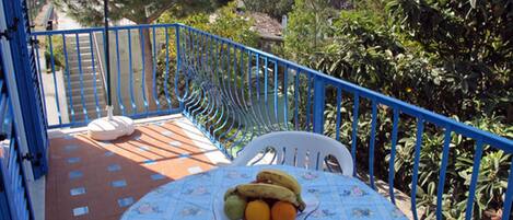 A balcony with a table set for two, a chair, and a fruit bowl.