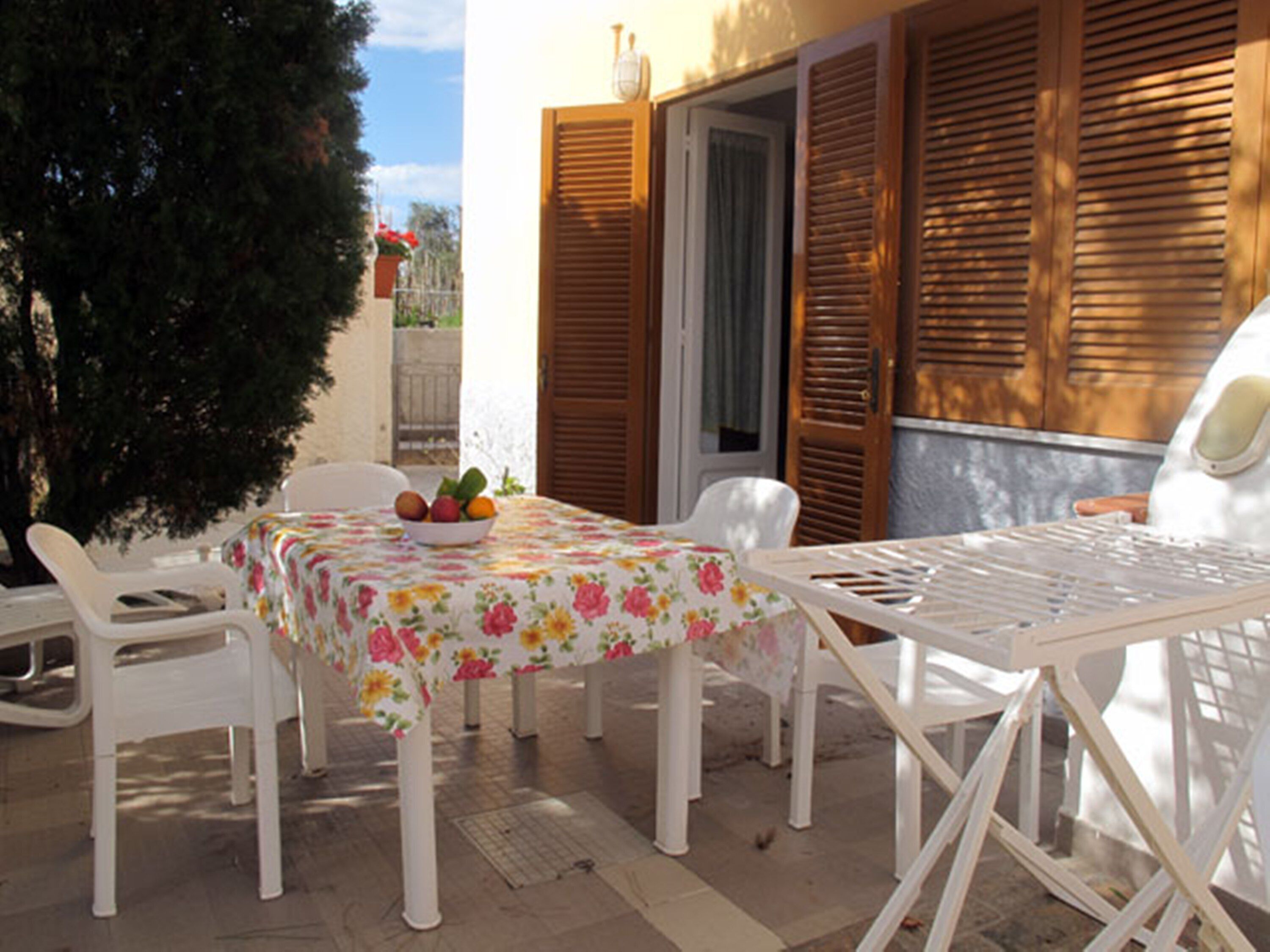 A patio with a table and chairs, a bowl of fruit, and wooden shutters.