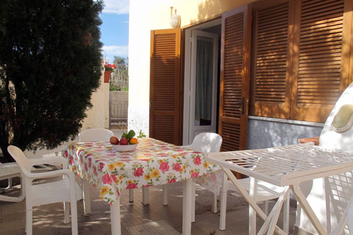 A patio with a table and chairs, a bowl of fruit, and wooden shutters.
