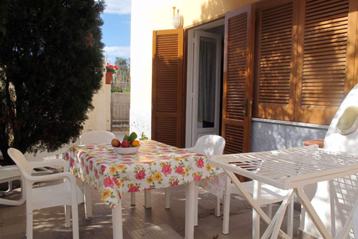 A patio with a table and chairs, a bowl of fruit, and wooden shutters.