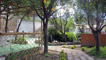 Un jardín con un sendero empedrado, un área cercada y árboles frutales.