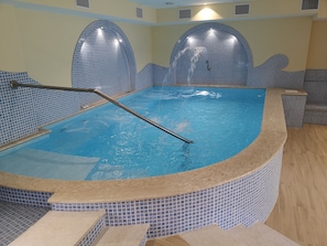 An indoor swimming pool with a tiled interior, a metal ladder, and a tiled wall with a wave-like design. - Residence Villa Marinù (Forio)