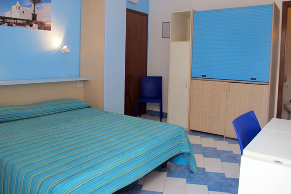 A room with a bed, a blue chair, a wardrobe, and a small table.