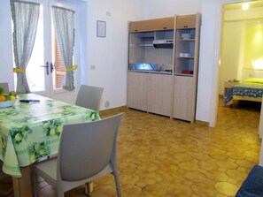 A dining area with a table covered by a green tablecloth, chairs, a kitchen area with cabinets, and a bedroom with a bed and a nightstand. - Residence Villa Marinù (Forio)
