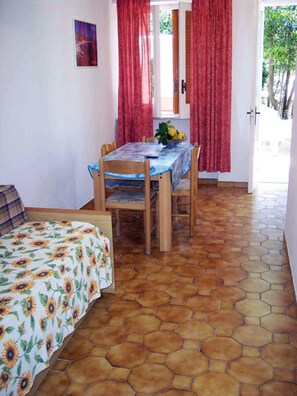 A room with a dining table, chairs, a bed with a floral bedspread, and a tiled floor. - Residence Villa Marinù (Forio)