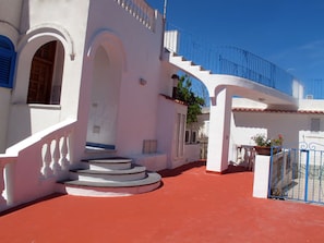 A white building with a red-tiled roof, a blue gate, and a staircase leading to a second floor. - Residence Villa Marinù (Forio)