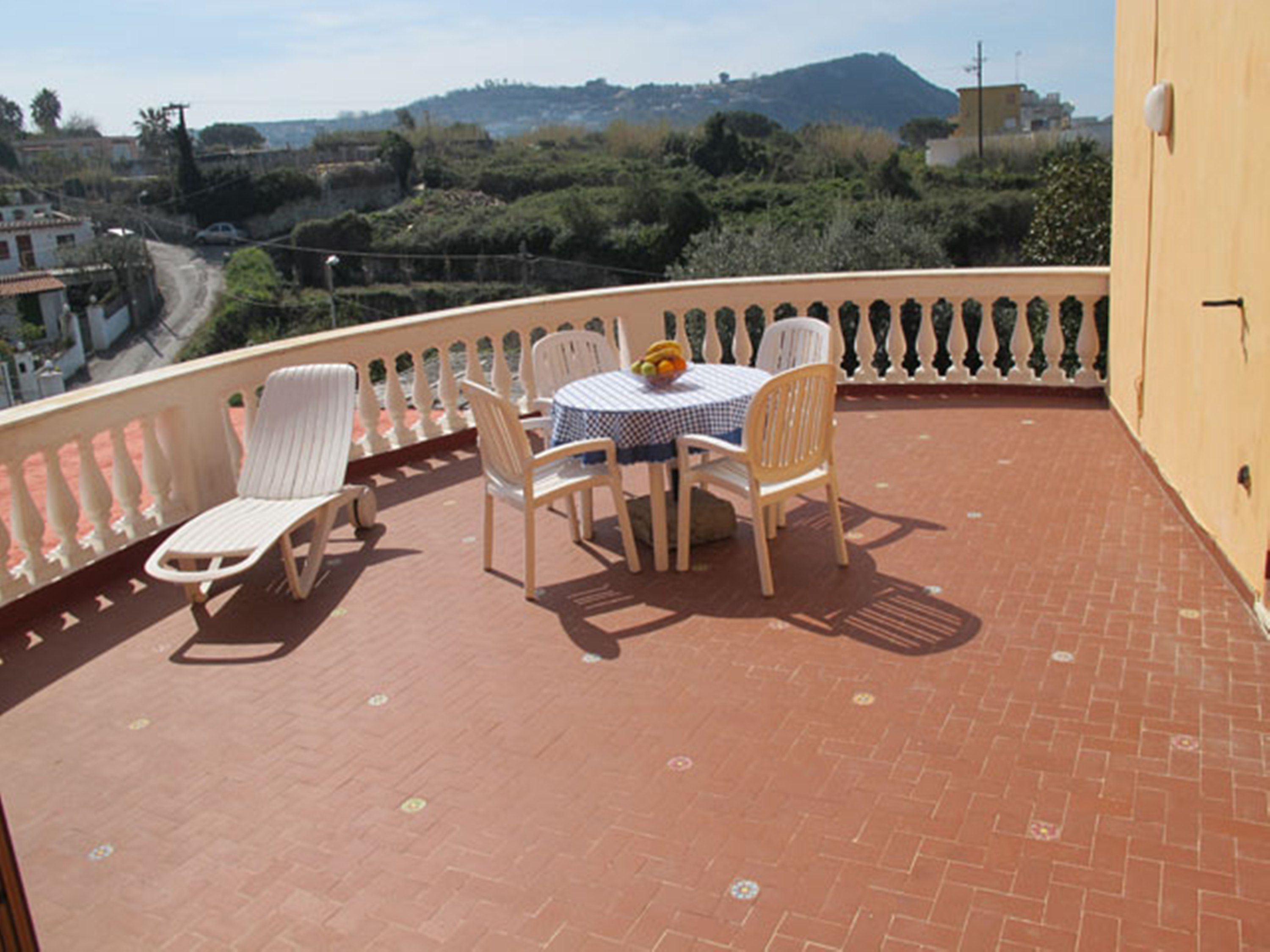 A balcony with a table and chairs, a view of the surrounding landscape, and a tiled floor.