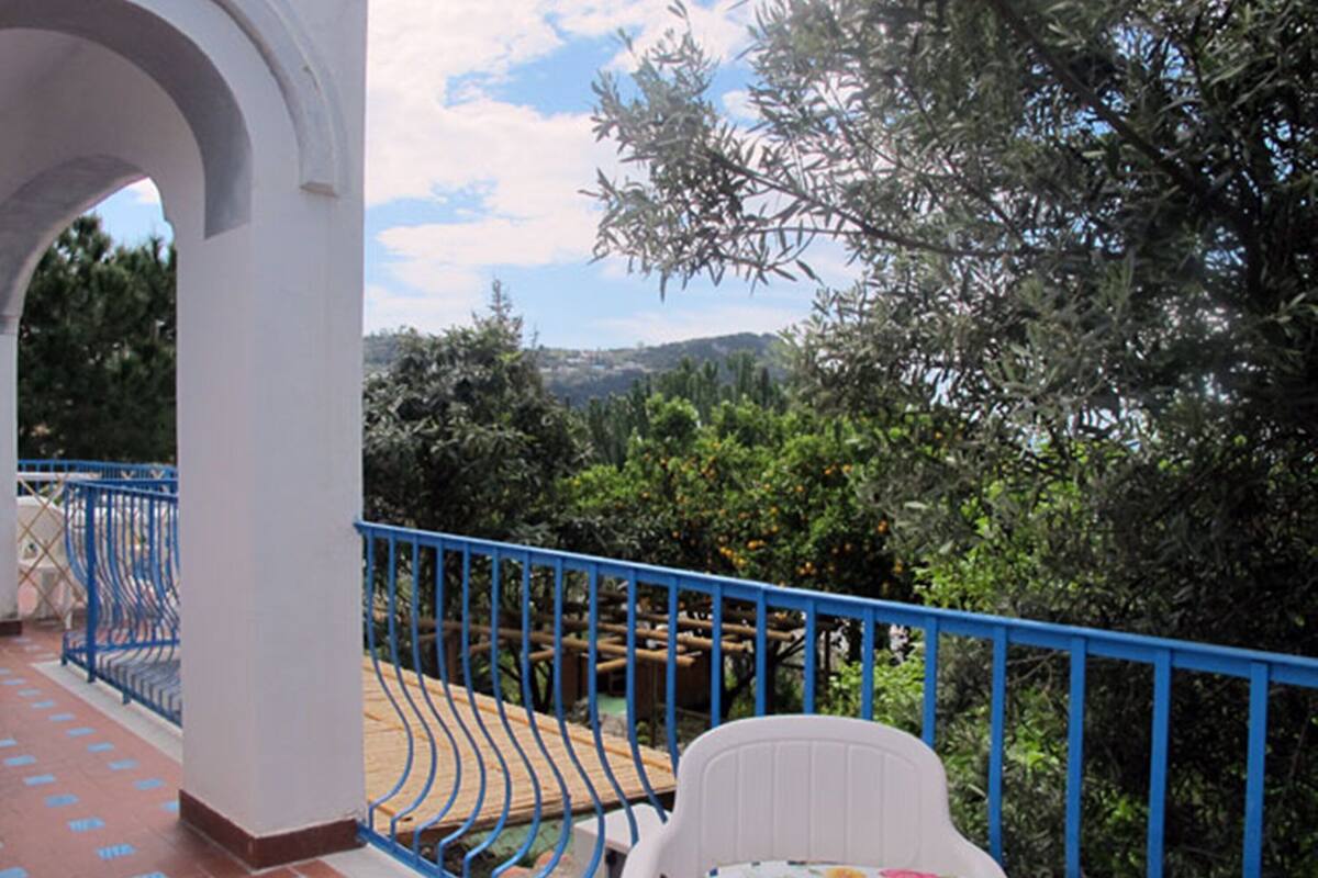 A balcony with a blue railing, a white chair, and a table with a floral tablecloth.