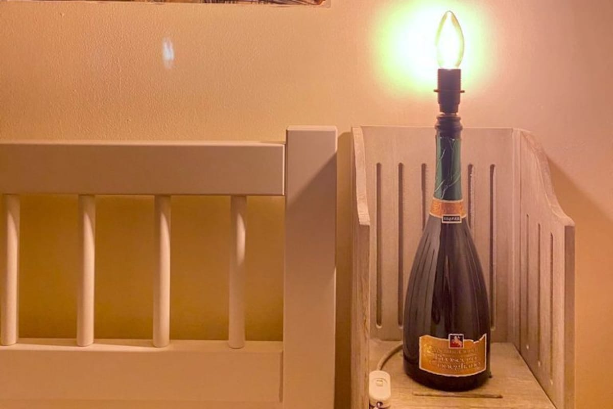 A bottle of wine on a wooden shelf with a lit candle in the background.