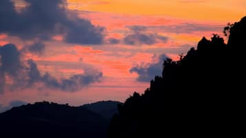 Un atardecer sobre un paisaje montañoso con siluetas de árboles y afloramientos rocosos.