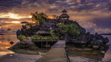 A secluded island with a thatched-roof structure, a wooden dock, and lush greenery.