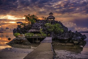 A secluded island with a thatched-roof structure, a wooden dock, and lush greenery. - Sangat Island Dive Resort (Coron)