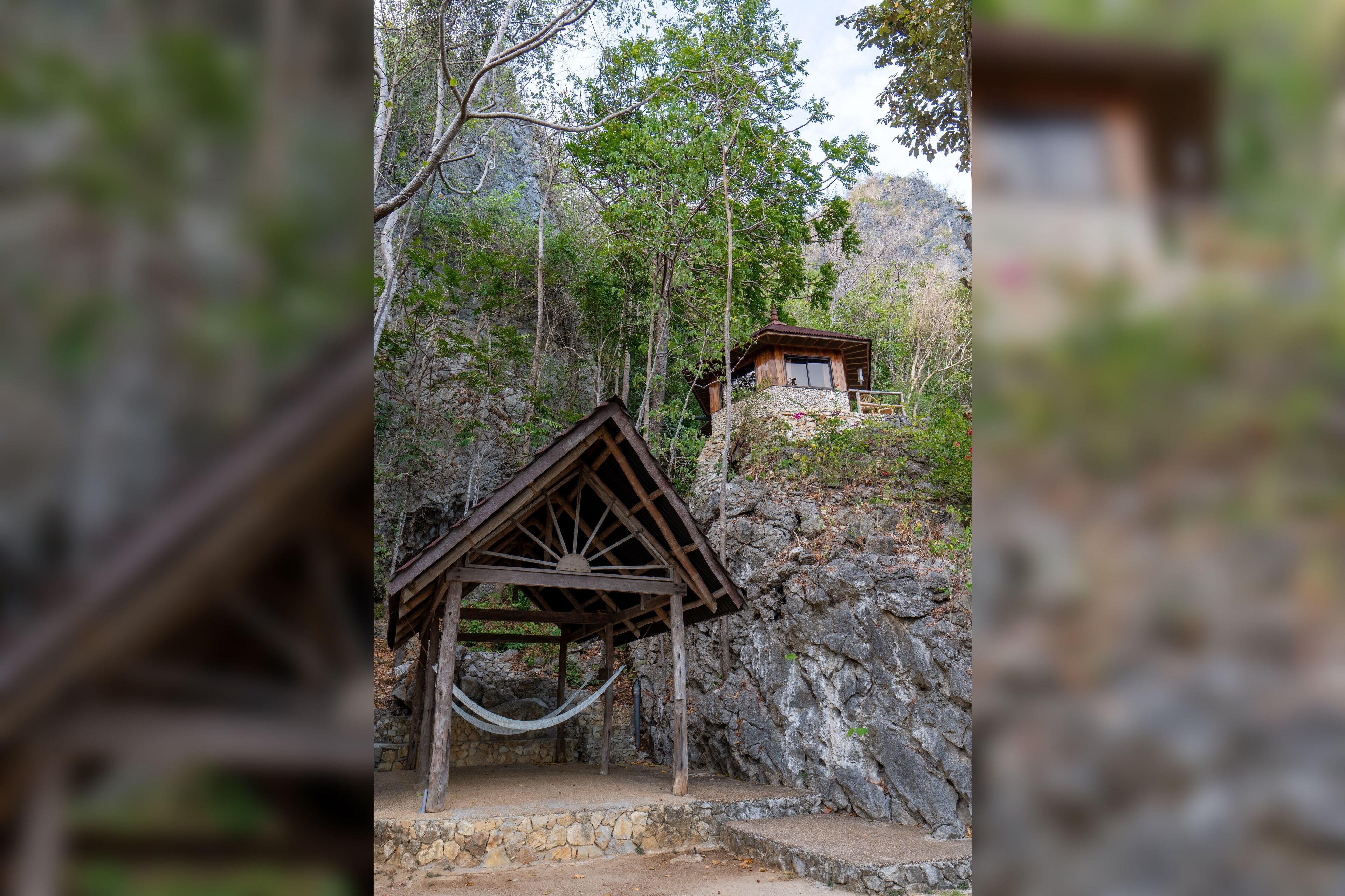 A wooden gazebo with a hammock, surrounded by trees and rocky terrain.
