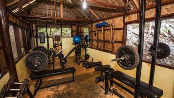 A gym with various weightlifting equipment, benches, and a thatched roof structure.