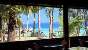 A beachside restaurant with outdoor seating, palm trees, and a view of the ocean. - Sangat Island Dive Resort (Coron)