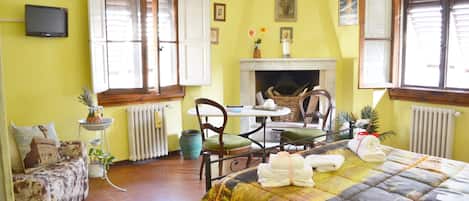 A room with a bed, a sofa, a dining table with chairs, a fireplace, and a TV mounted on the wall.
