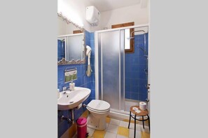 Une salle de bain équipée d’une douche, de toilettes, d’un lavabo et d’une petite table avec une chaise.