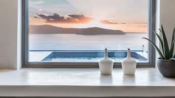 A window with a view of a sunset over water, two white vases, and a potted plant on a windowsill.