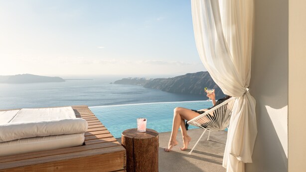 Una persona descansando en una silla junto a una piscina con vistas al mar y montañas.