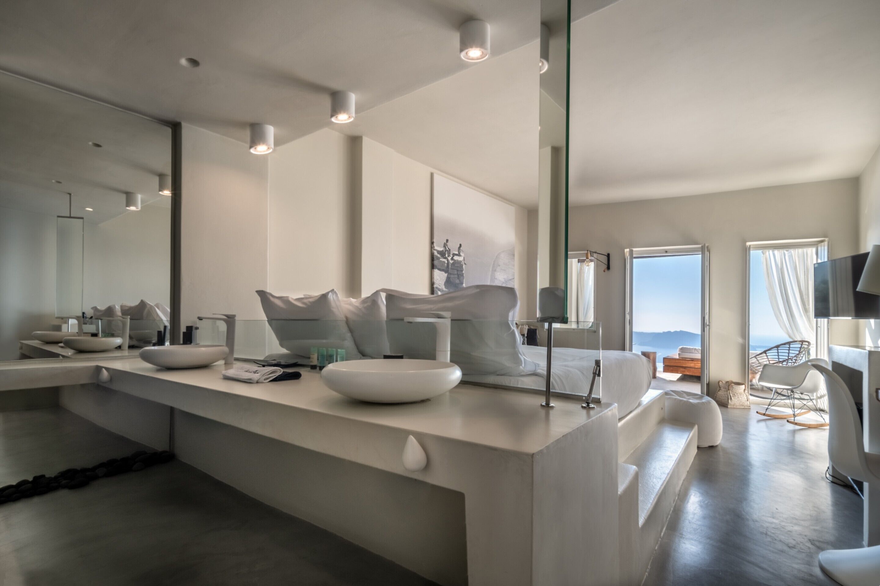 A modern bathroom with a large mirror, white fixtures, and a view of the sea.