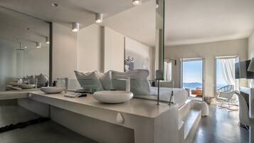 A modern bathroom with a large mirror, white fixtures, and a view of the sea.