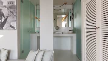 Un dormitorio con cama, almohadas, mesita de noche y espejo, además de un baño con lavabo y espejo.