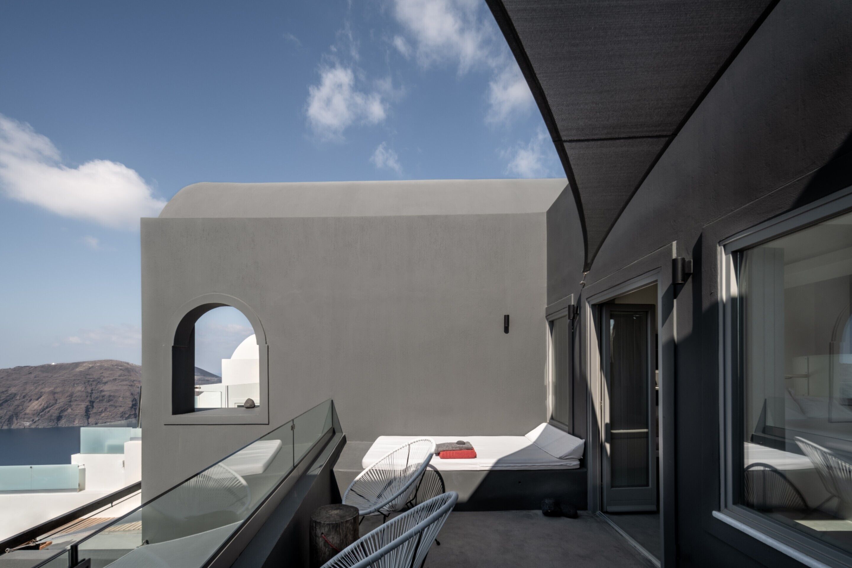 A balcony with a view of the sea, a white wall, and a door leading to an interior space.